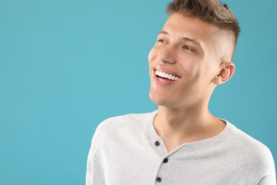 Photo of Happy young man on light blue background, space for text. Dental veneers