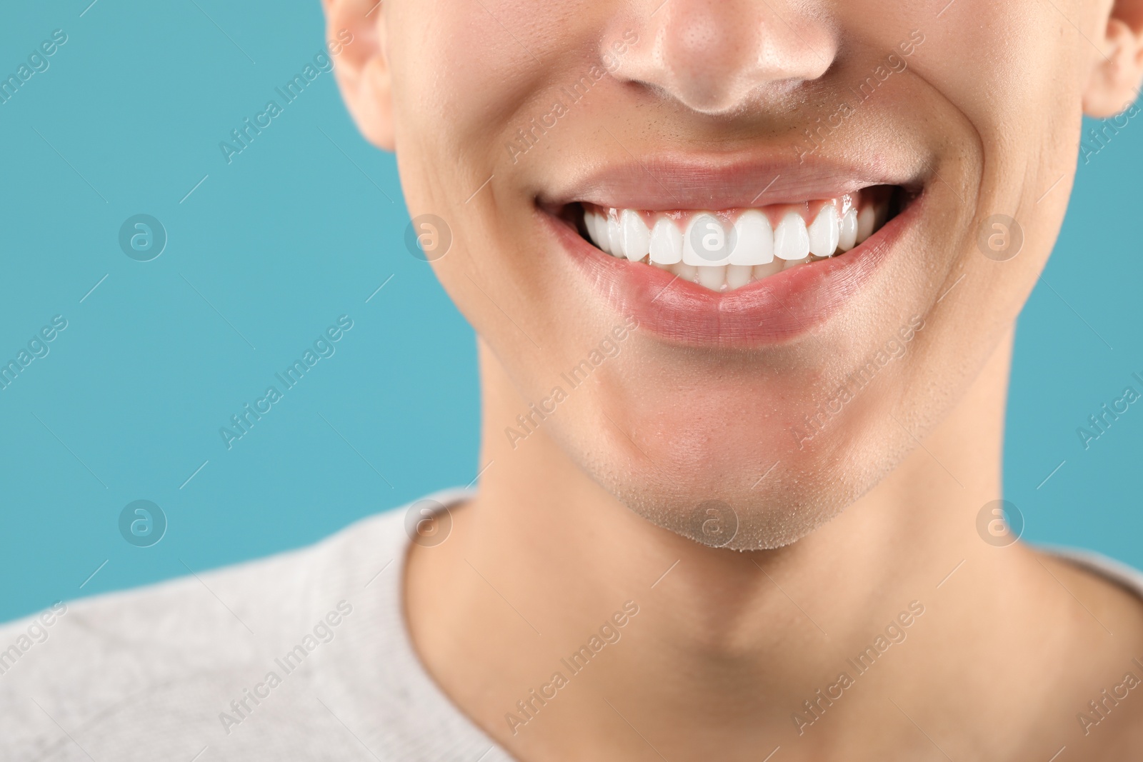 Photo of Happy young man on light blue background, closeup. Dental veneers