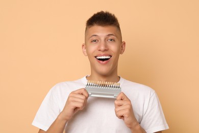 Photo of Happy young man with teeth color samples on beige background. Dental veneers