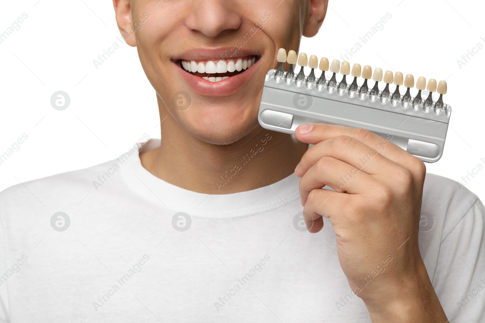 Photo of Happy young man with teeth color samples on white background, closeup. Dental veneers