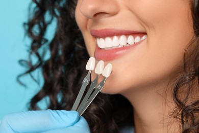 Photo of Doctor checking young woman's teeth color on light blue background, closeup. Dental veneers