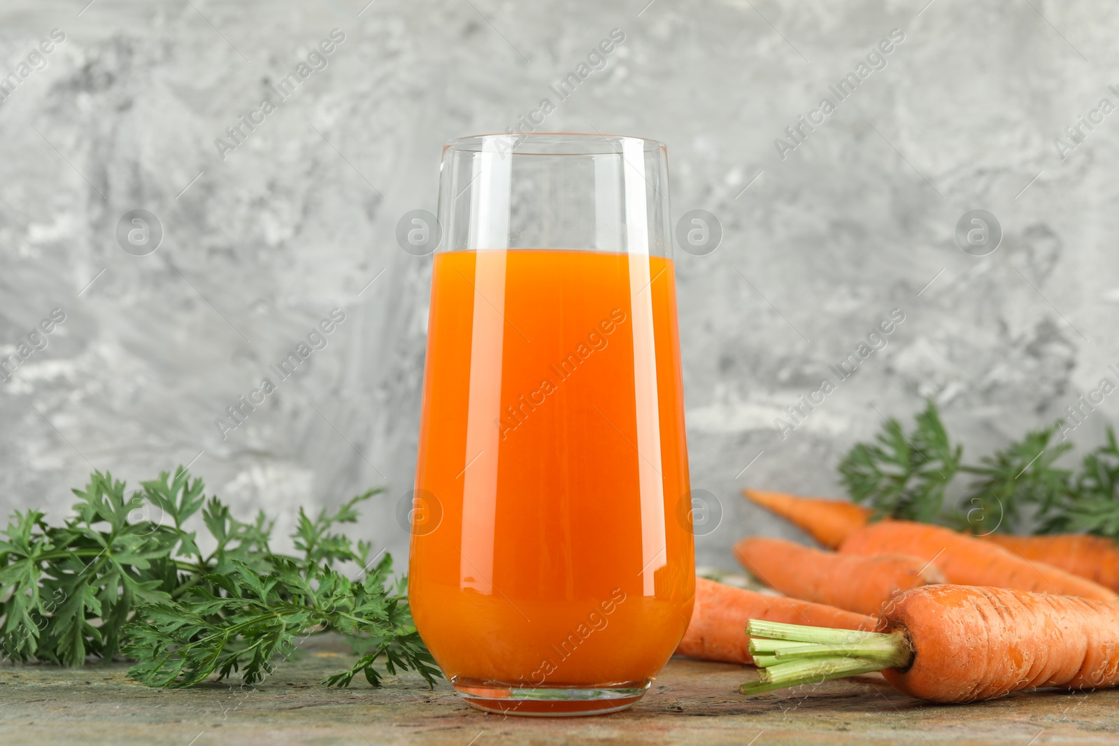 Photo of Fresh carrot juice in glass and vegetables on textured table