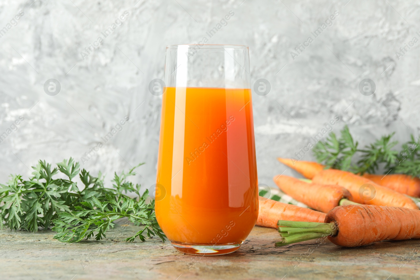 Photo of Fresh carrot juice in glass and vegetables on textured table