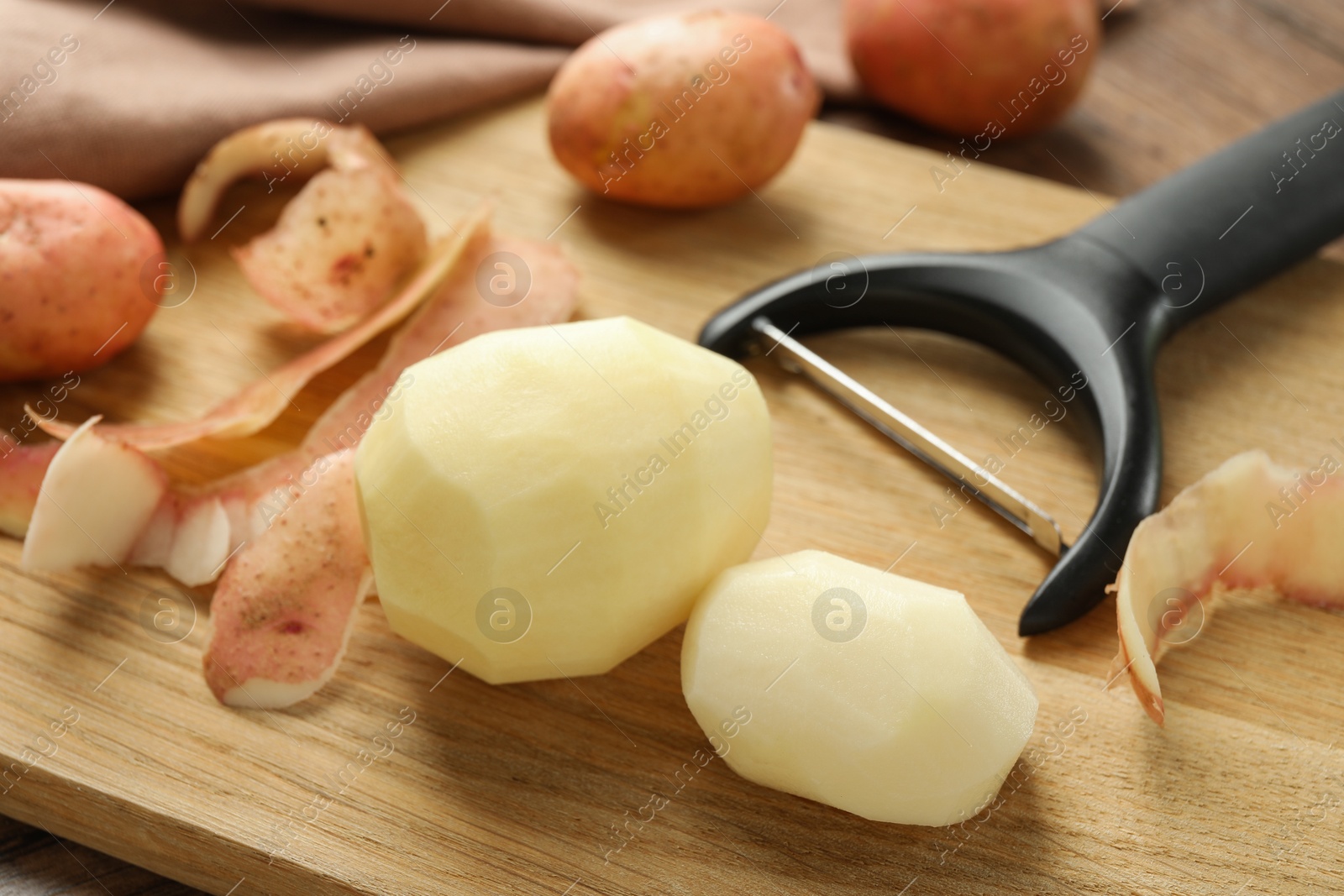 Photo of Fresh raw potatoes, peels and peeler on wooden table, closeup