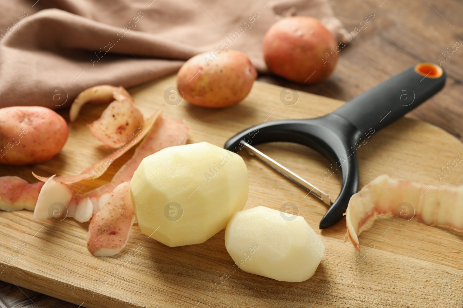 Photo of Fresh raw potatoes, peels and peeler on wooden table, closeup