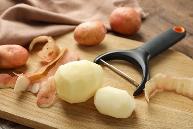 Photo of Fresh raw potatoes, peels and peeler on wooden table, closeup