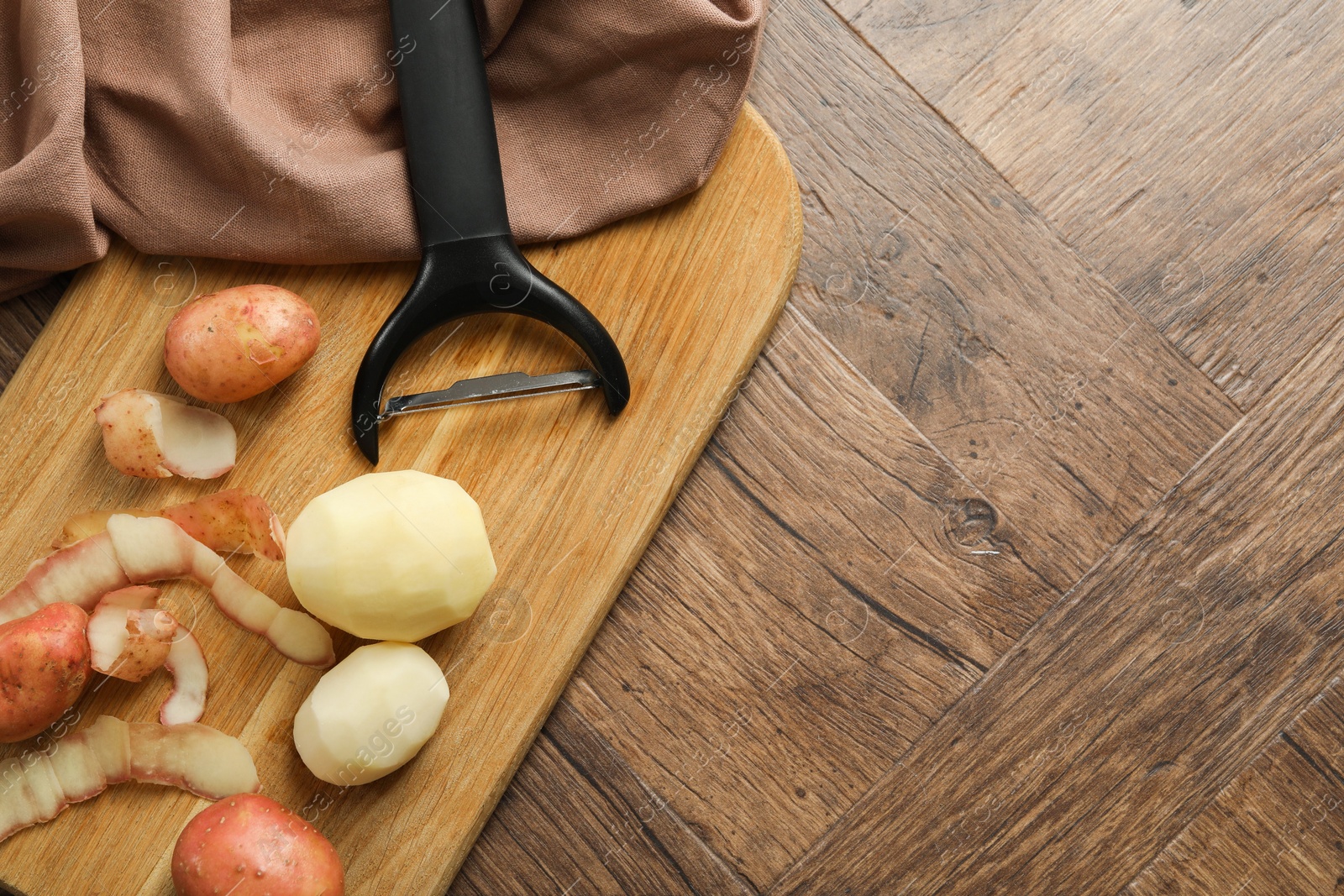 Photo of Fresh raw potatoes, peels and peeler on wooden table, top view. Space for text