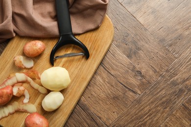 Photo of Fresh raw potatoes, peels and peeler on wooden table, top view. Space for text