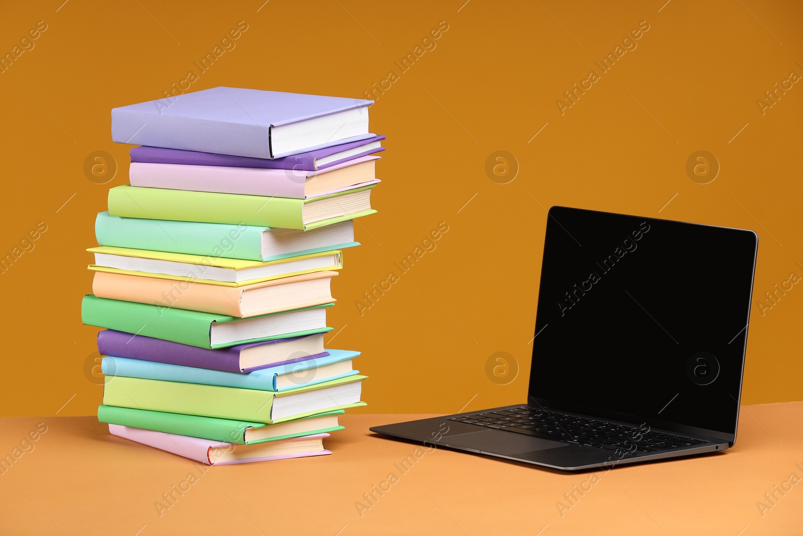 Photo of Stack of colorful books and laptop on orange background