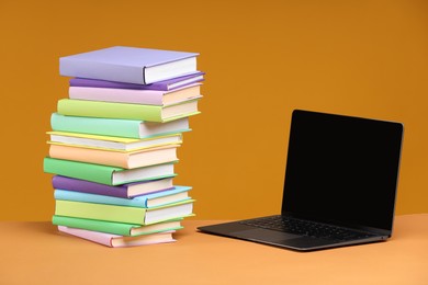 Stack of colorful books and laptop on orange background