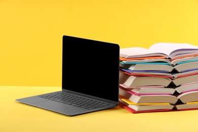 Photo of Stack of colorful books and laptop on yellow background