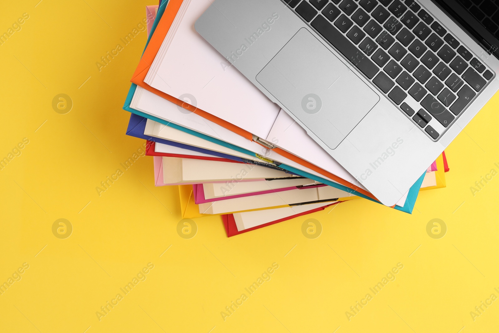 Photo of Stack of colorful books and laptop on yellow background, top view