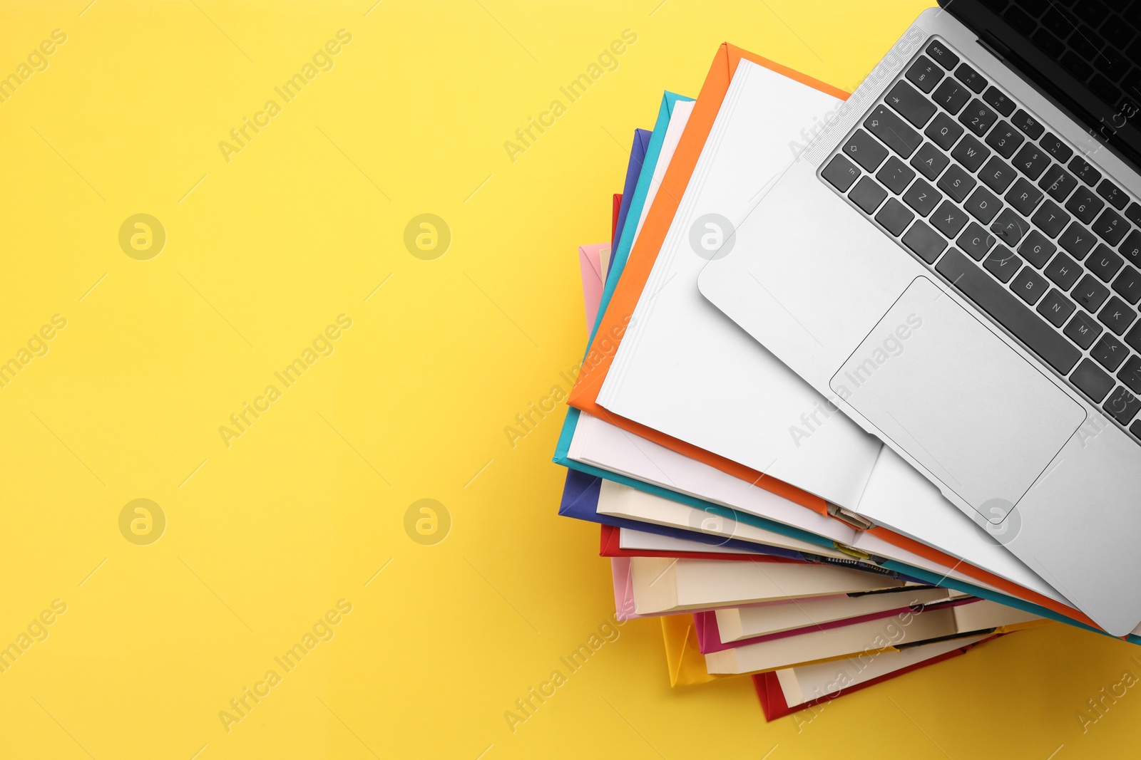 Photo of Stack of colorful books and laptop on yellow background, top view. Space for text