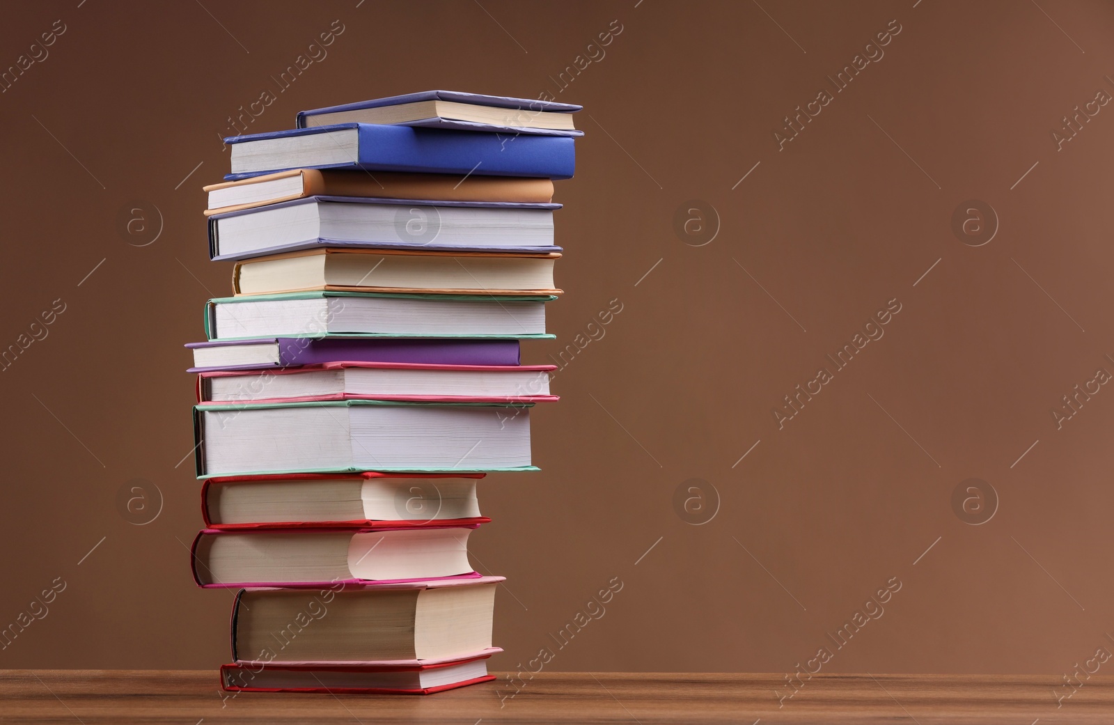 Photo of Stack of colorful books on wooden table against light brown background, space for text