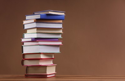 Photo of Stack of colorful books on wooden table against light brown background, space for text