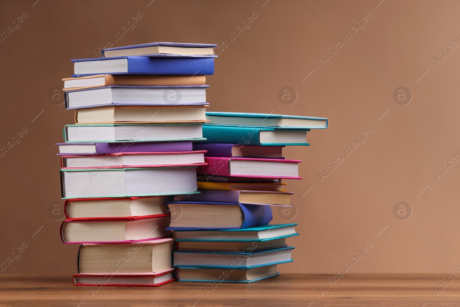 Photo of Stacks of colorful books on wooden table against light brown background, space for text