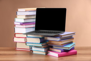 Photo of Stacks of colorful books and laptop on wooden table against light brown background