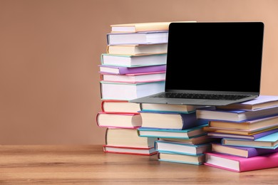 Photo of Stacks of colorful books and laptop on wooden table against light brown background, space for text