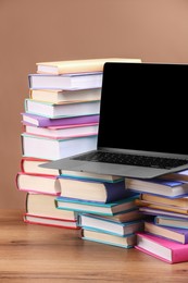 Photo of Stacks of colorful books and laptop on wooden table against light brown background