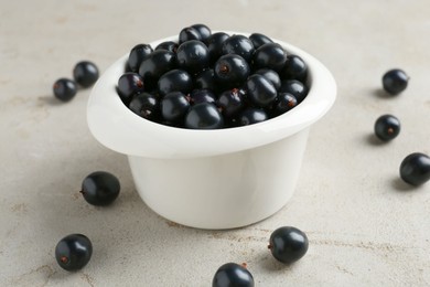 Ripe black currants in bowl on light table, closeup