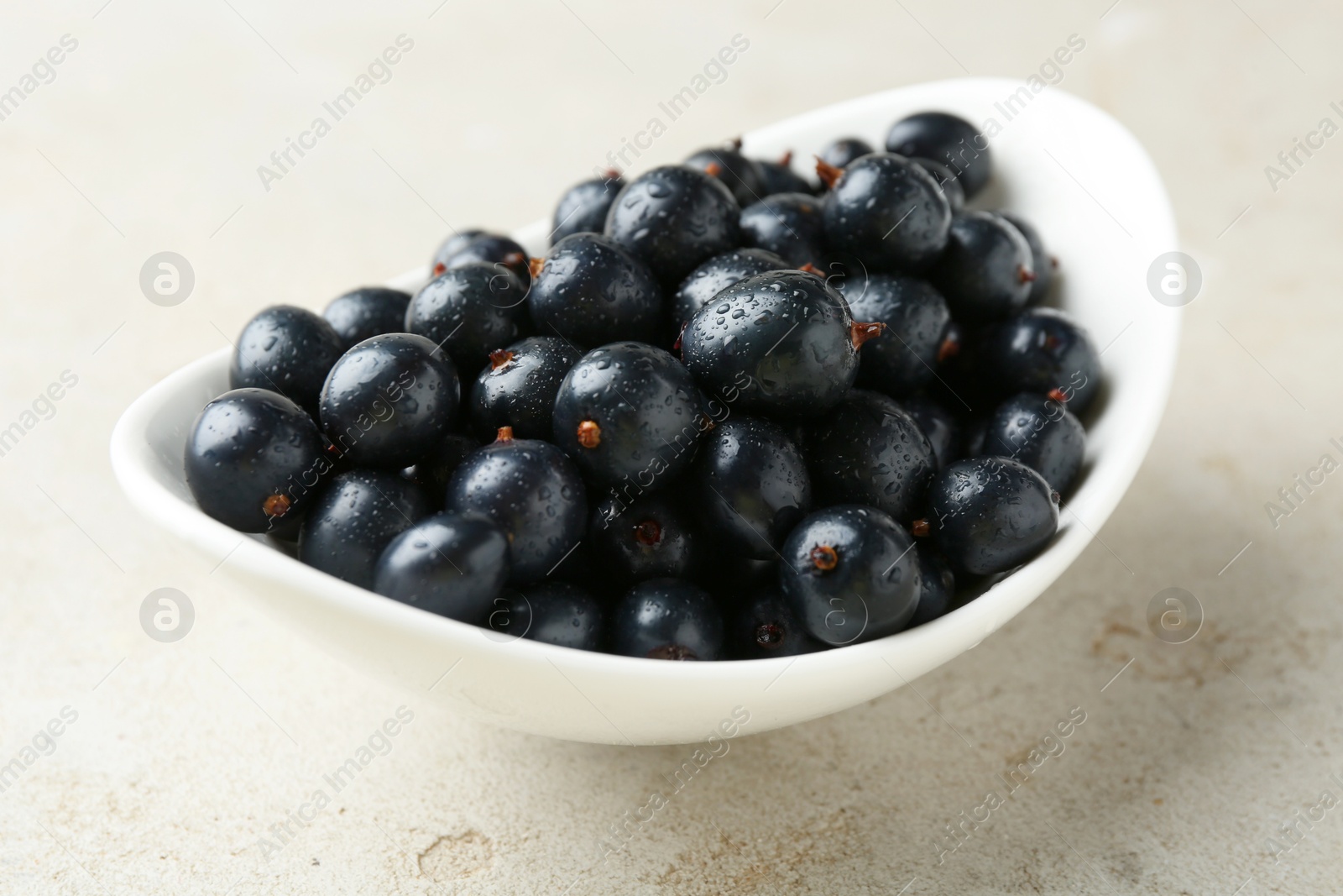 Photo of Ripe black currants in bowl on light table, closeup