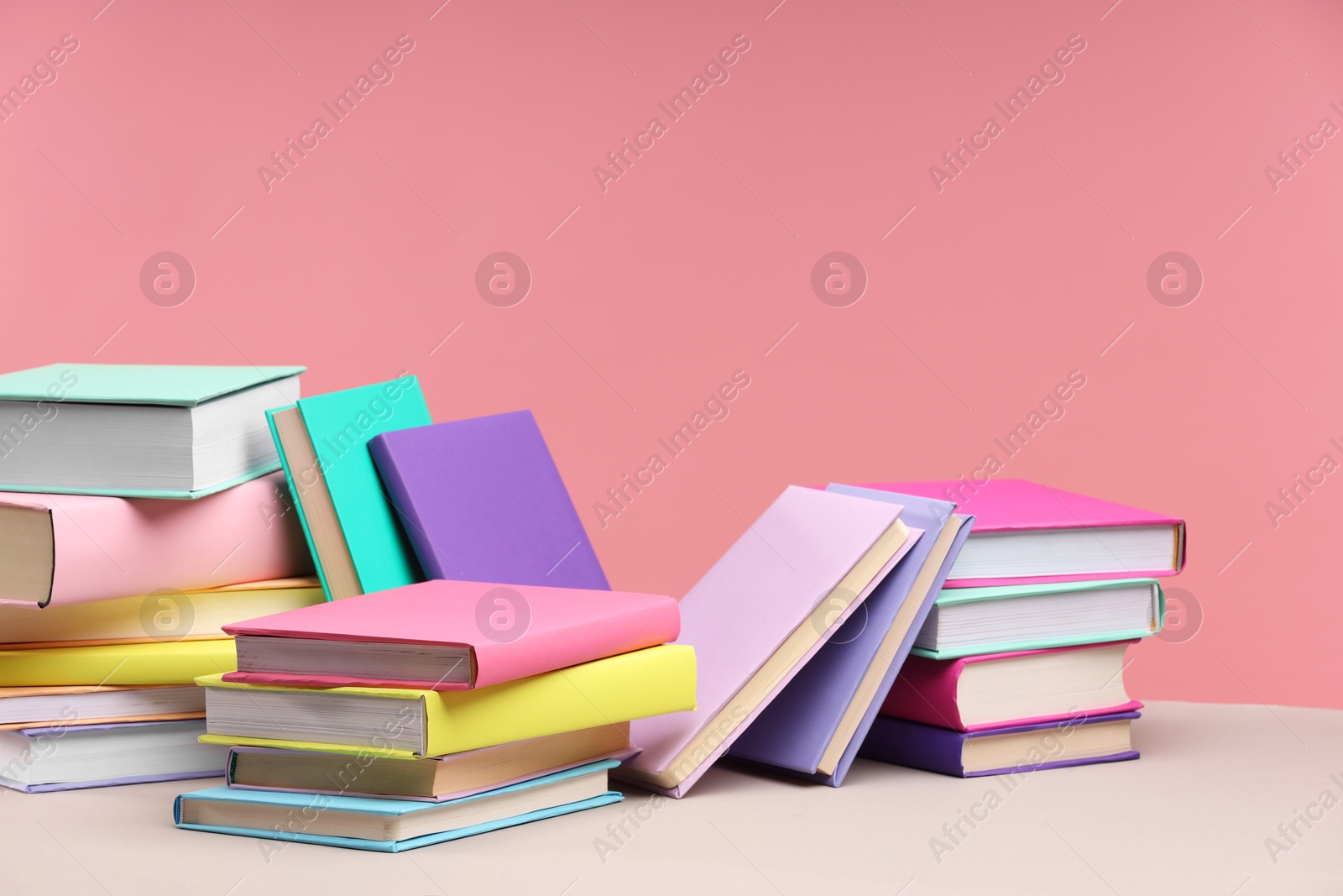 Photo of Many colorful books on beige table against pink background, space for text