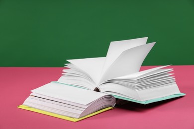 Photo of Colorful books on pink table against green background