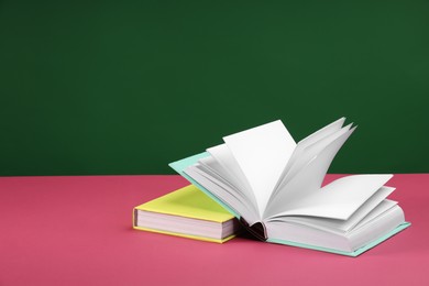 Colorful books on pink table against green background, space for text