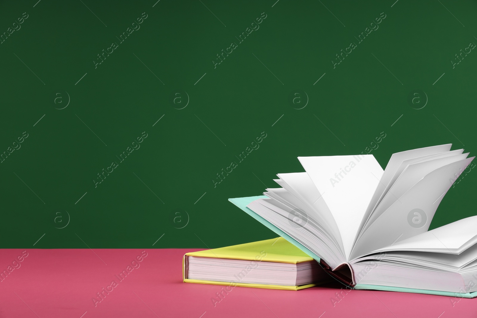 Photo of Colorful books on pink table against green background, space for text