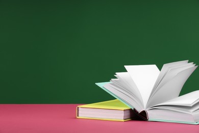 Photo of Colorful books on pink table against green background, space for text