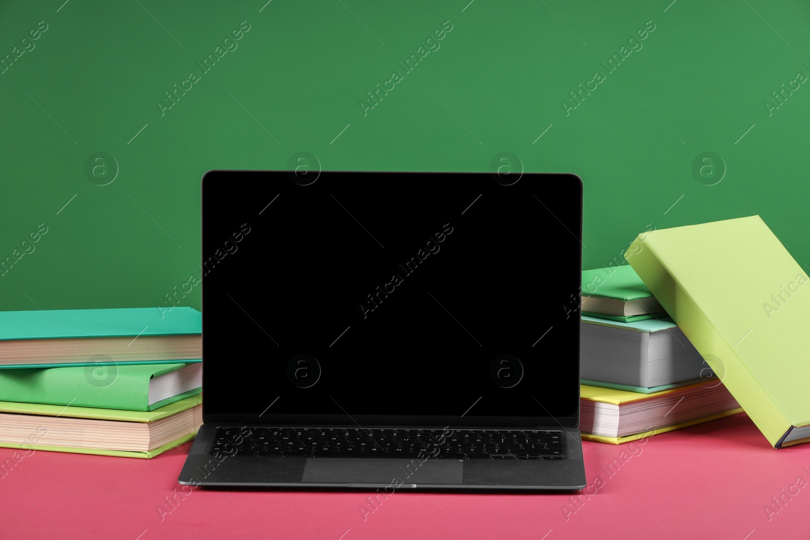 Photo of Many colorful books and laptop on pink table against green background