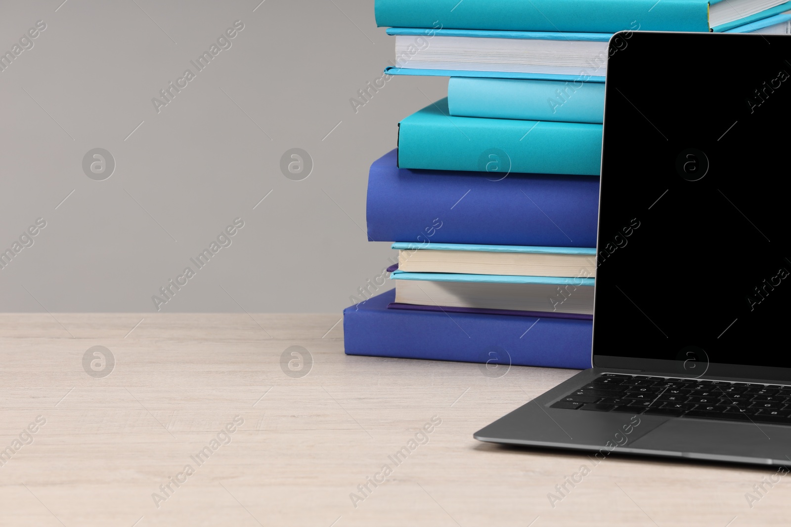 Photo of Stack of colorful books and laptop on white wooden table against light grey background, space for text