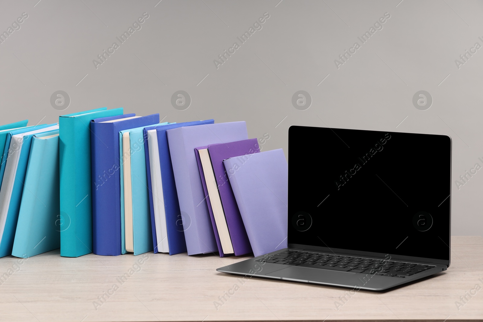 Photo of Colorful books and laptop on white wooden table against light grey background