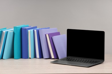 Colorful books and laptop on white wooden table against light grey background