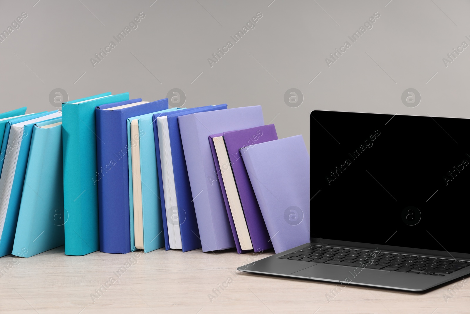 Photo of Colorful books and laptop on white wooden table against light grey background