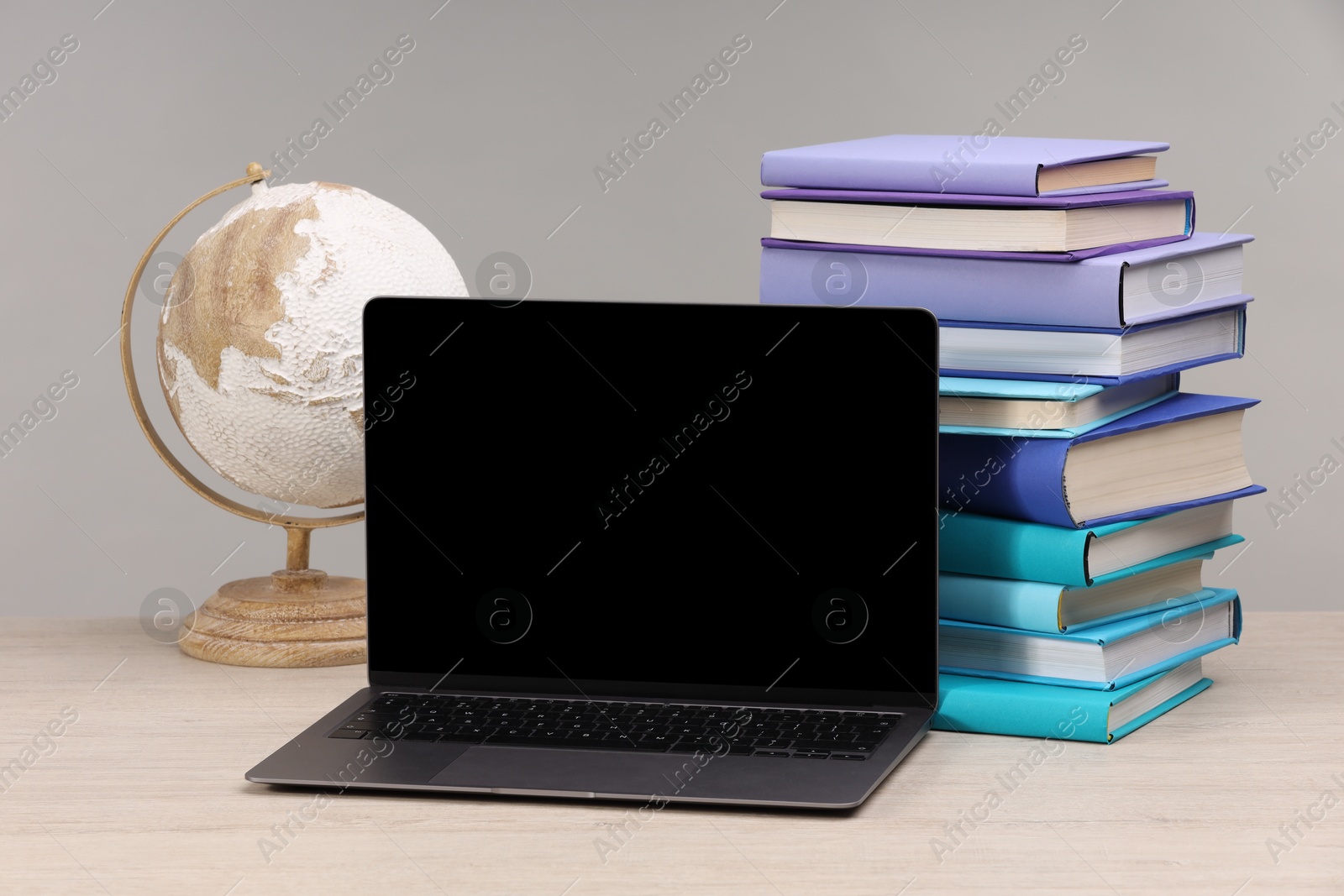 Photo of Stack of colorful books, globe and laptop on white wooden table against light grey background