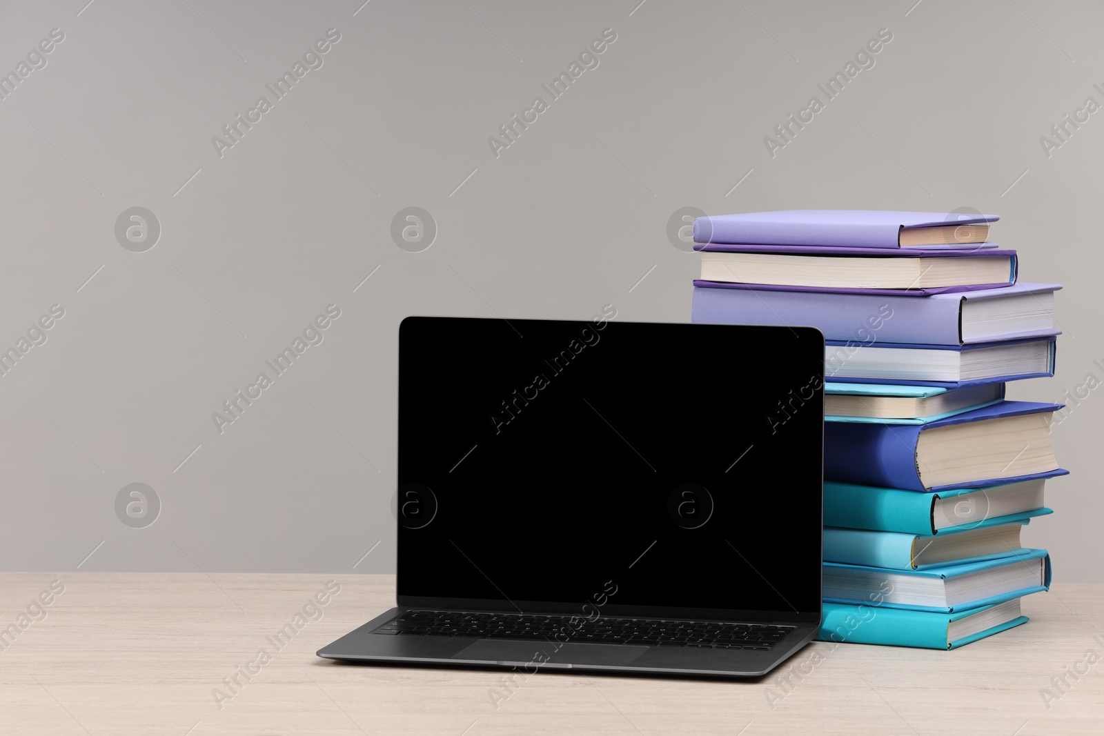 Photo of Stack of colorful books and laptop on white wooden table against light grey background