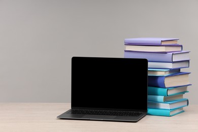 Stack of colorful books and laptop on white wooden table against light grey background