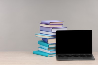 Photo of Stack of colorful books and laptop on white wooden table against light grey background, space for text