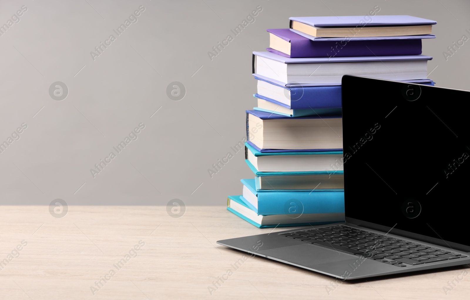 Photo of Stack of colorful books and laptop on white wooden table against light grey background, space for text