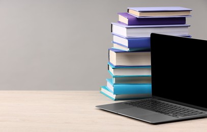 Photo of Stack of colorful books and laptop on white wooden table against light grey background, space for text