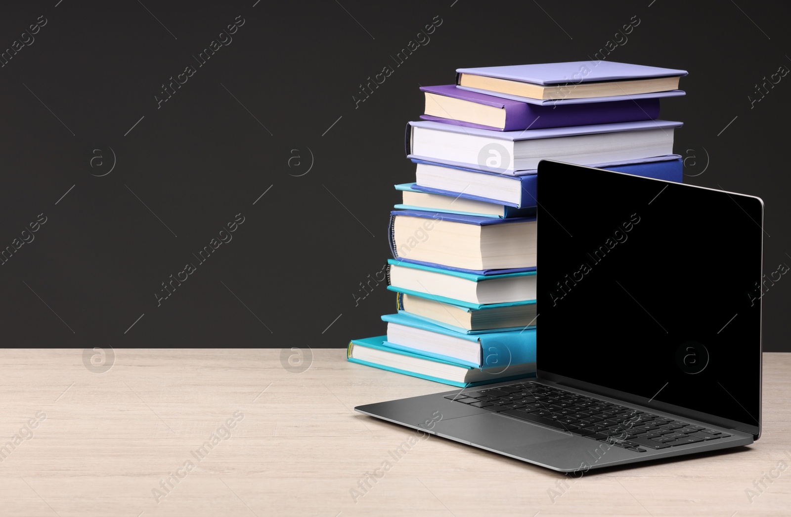 Photo of Stack of colorful books and laptop on white wooden table against black background, space for text