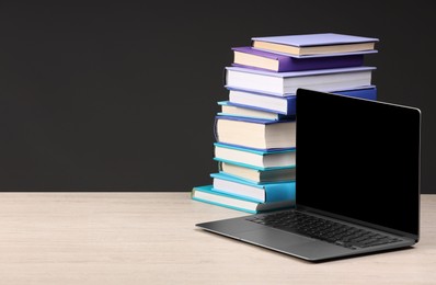 Photo of Stack of colorful books and laptop on white wooden table against black background, space for text