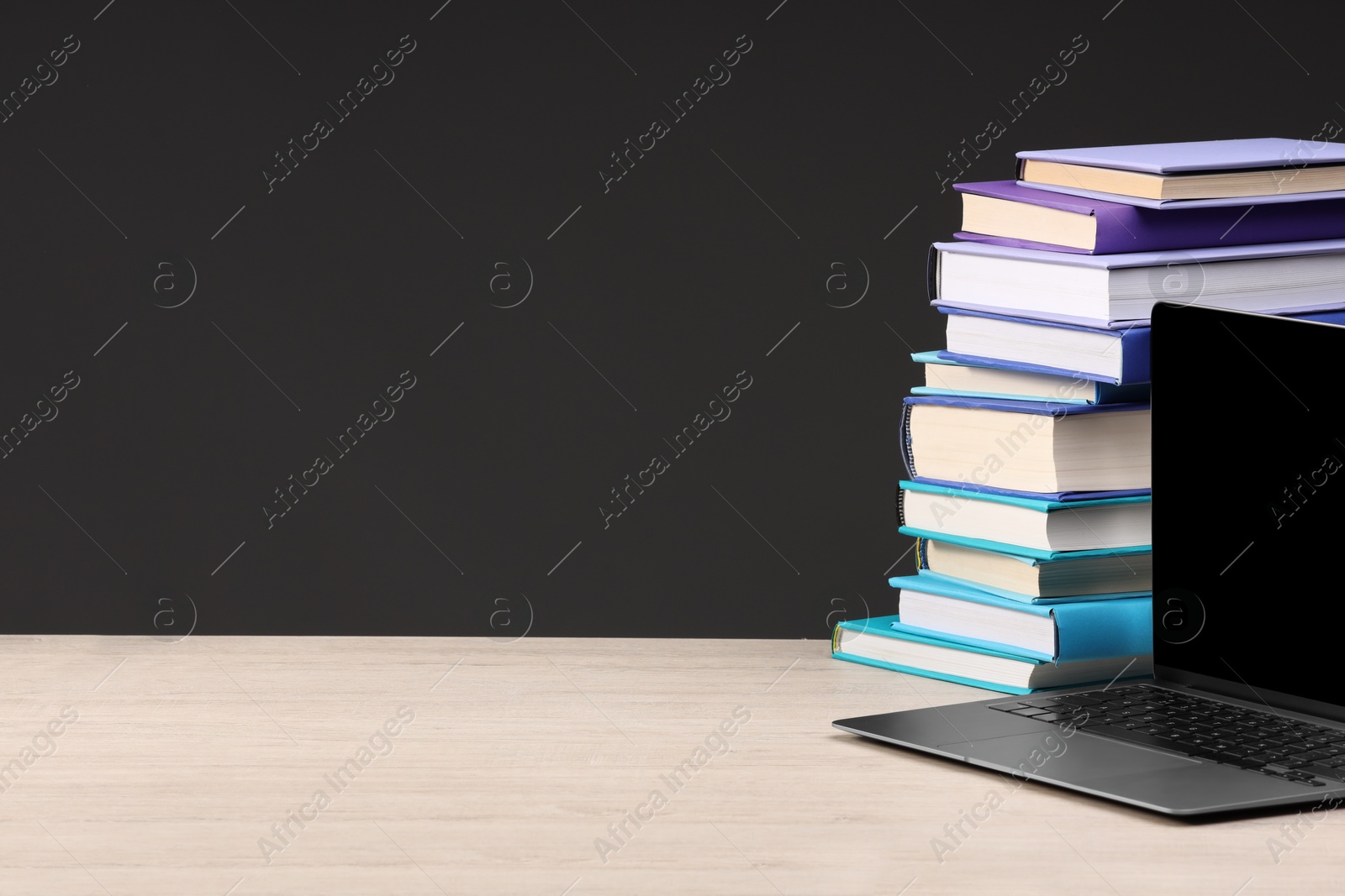 Photo of Stack of colorful books and laptop on white wooden table against black background, space for text