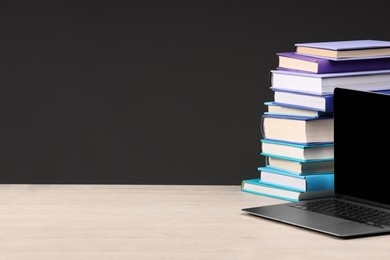 Photo of Stack of colorful books and laptop on white wooden table against black background, space for text