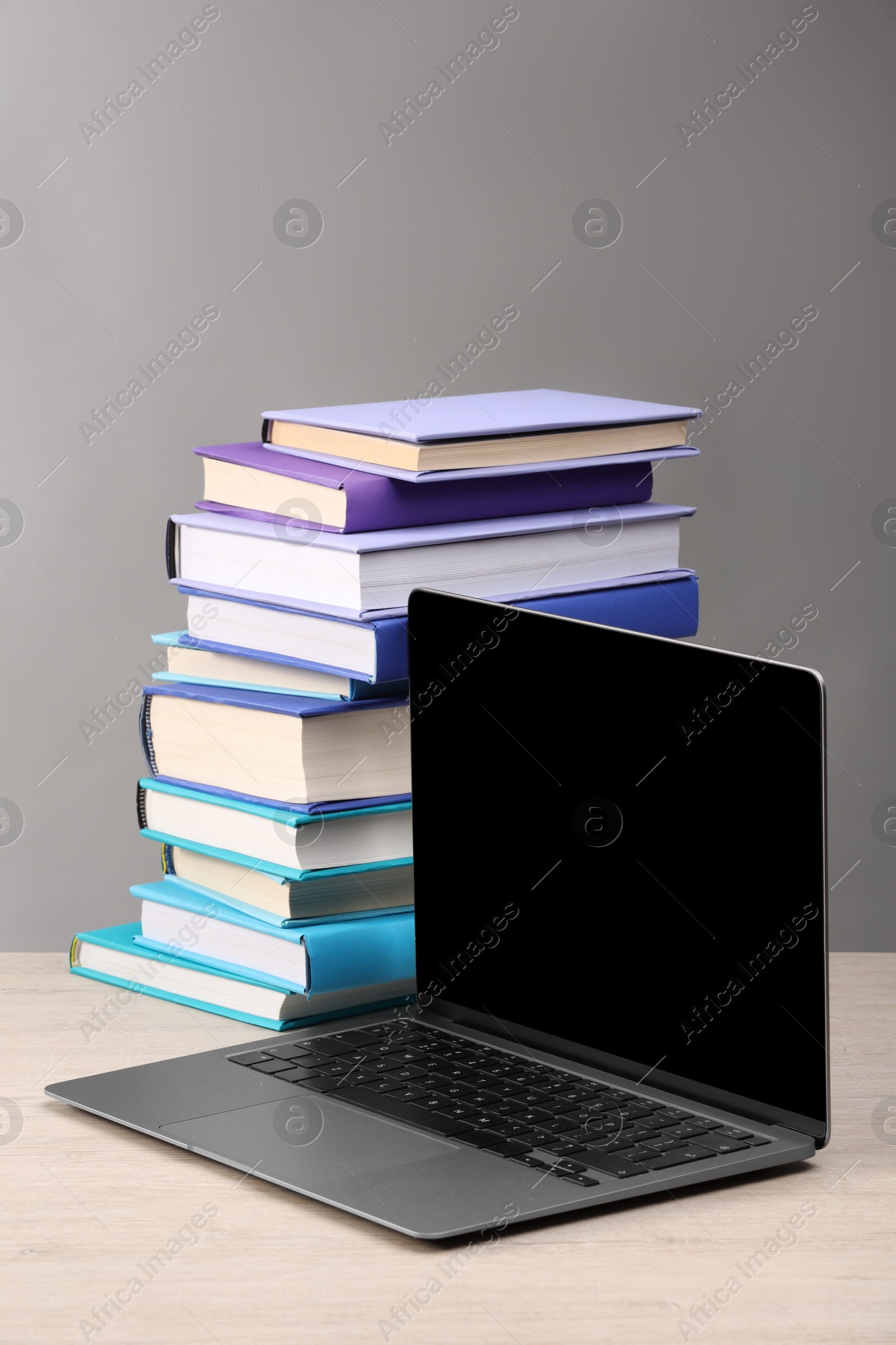 Photo of Stack of colorful books and laptop on white wooden table against light grey background