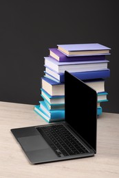 Stack of colorful books and laptop on white wooden table against black background