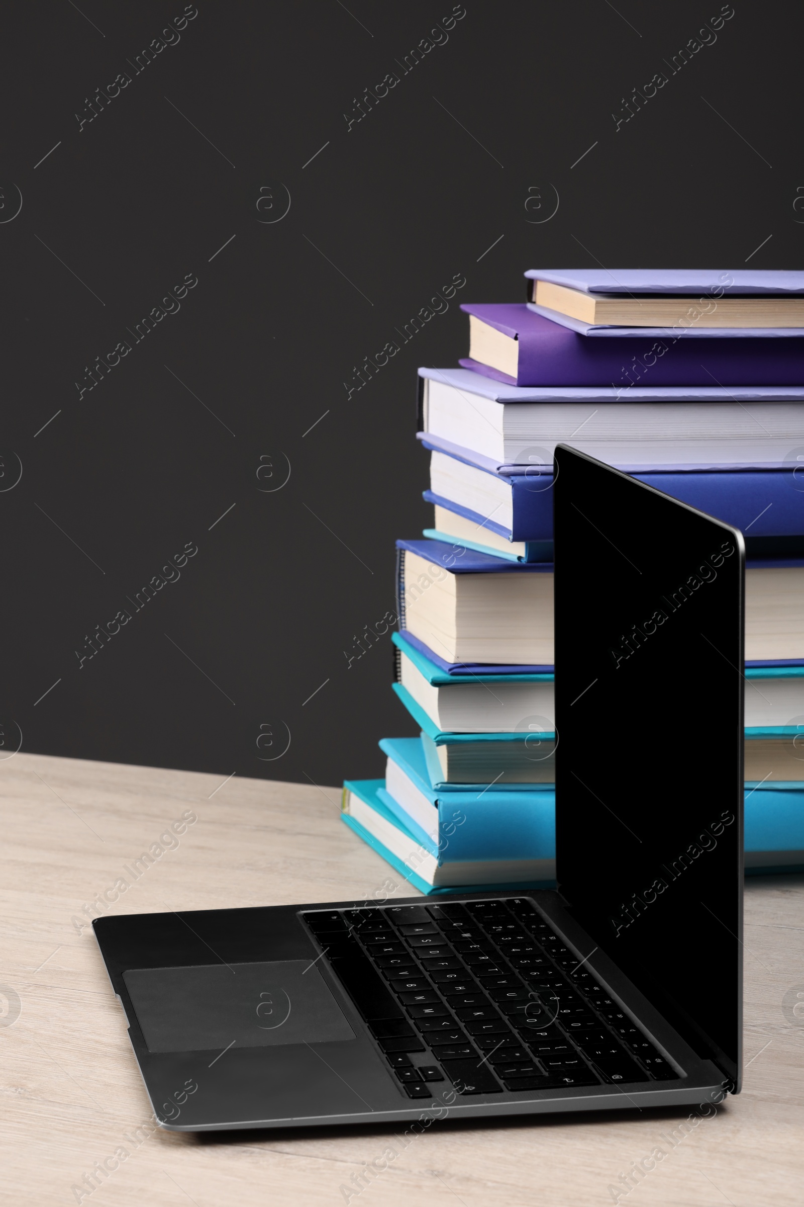 Photo of Stack of colorful books and laptop on white wooden table against black background