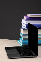 Stack of colorful books and laptop on white wooden table against black background