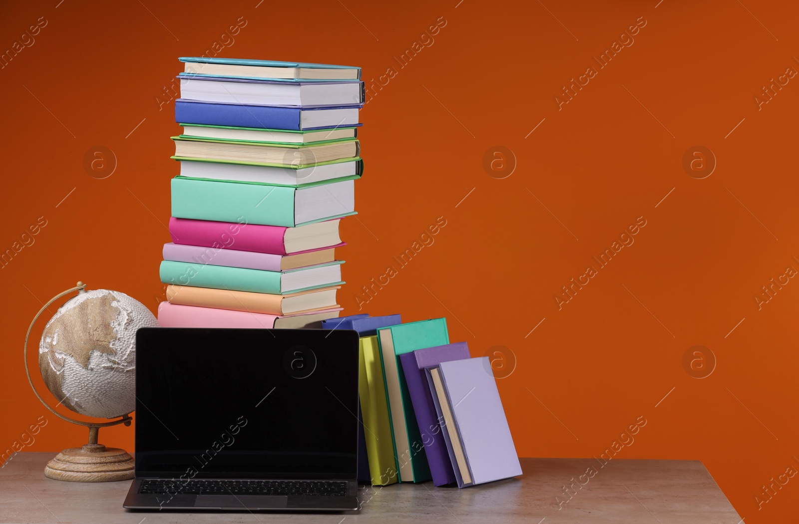 Photo of Stack of colorful books, globe and laptop on wooden table against orange background, space for text